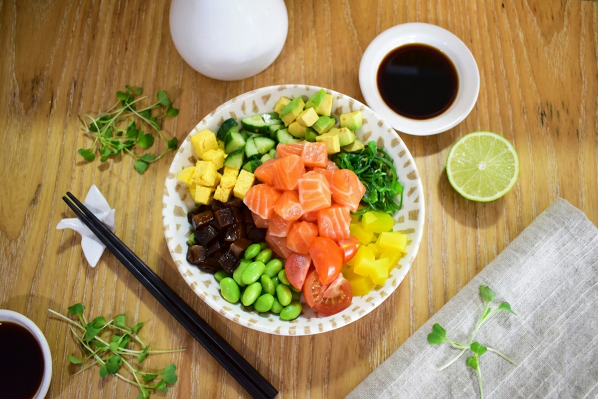 A poke bowl of salmon, edamame, avocado, and tomato on a wooden table