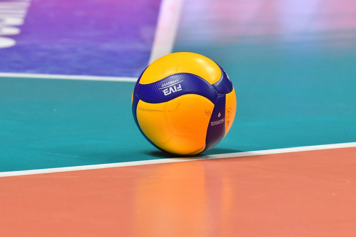 A yellow and blue volleyball resting on an indoor court line