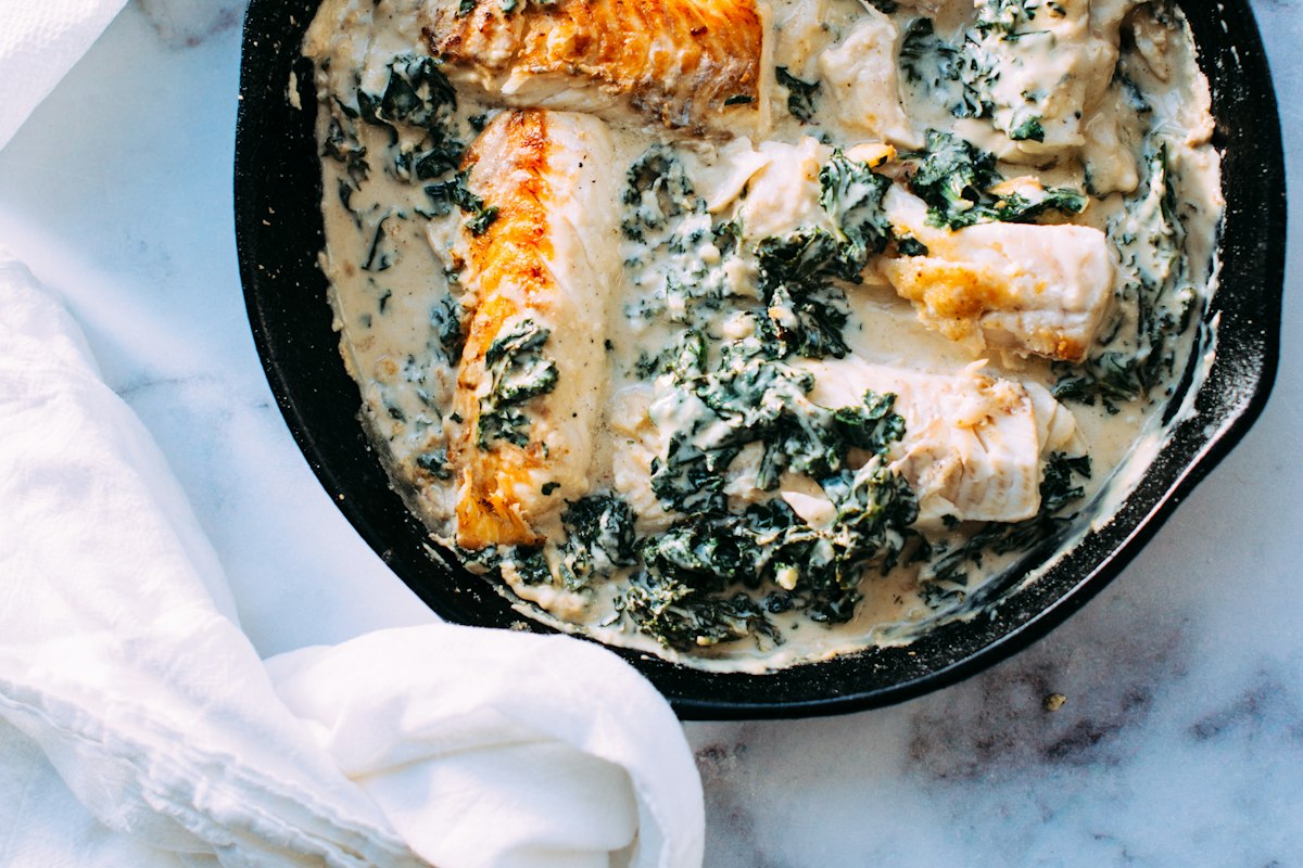 Seared fish and greens in a creamy sauce in a cast-iron pan
