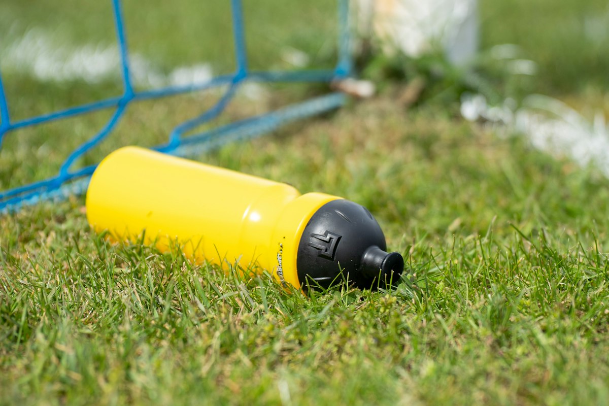 A yellow squeeze bottle lying in the grass beside a goal net