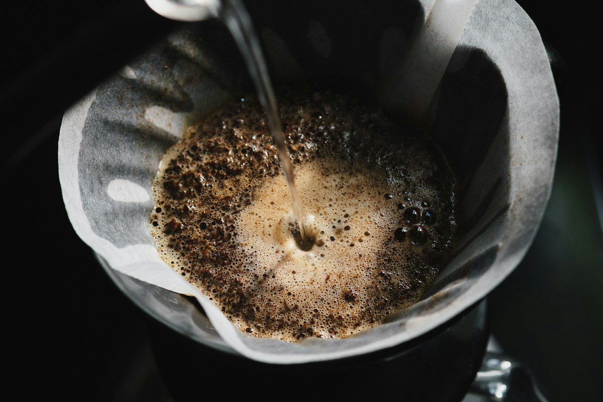 Water poured over ground coffee in a paper filter, in low light