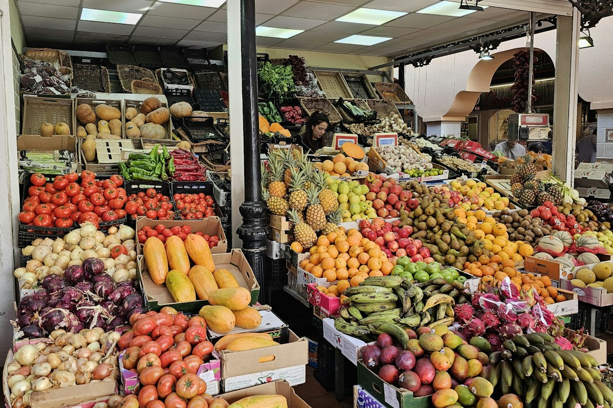 A market stall stacked with tomatoes, papaya, oranges, pineapples, and bananas