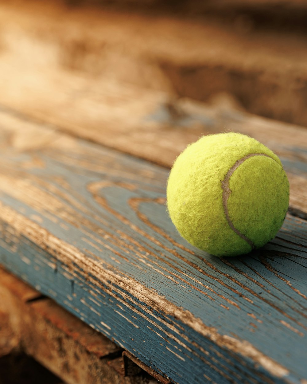 A tennis ball on a weathered wooden bench