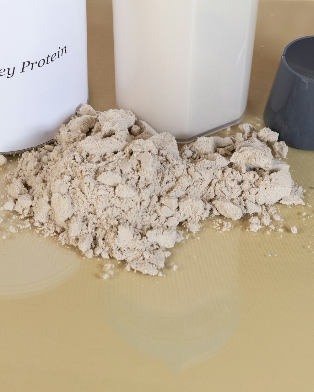 Whey powder, a tub, a shaker, and a scoop on a beige counter