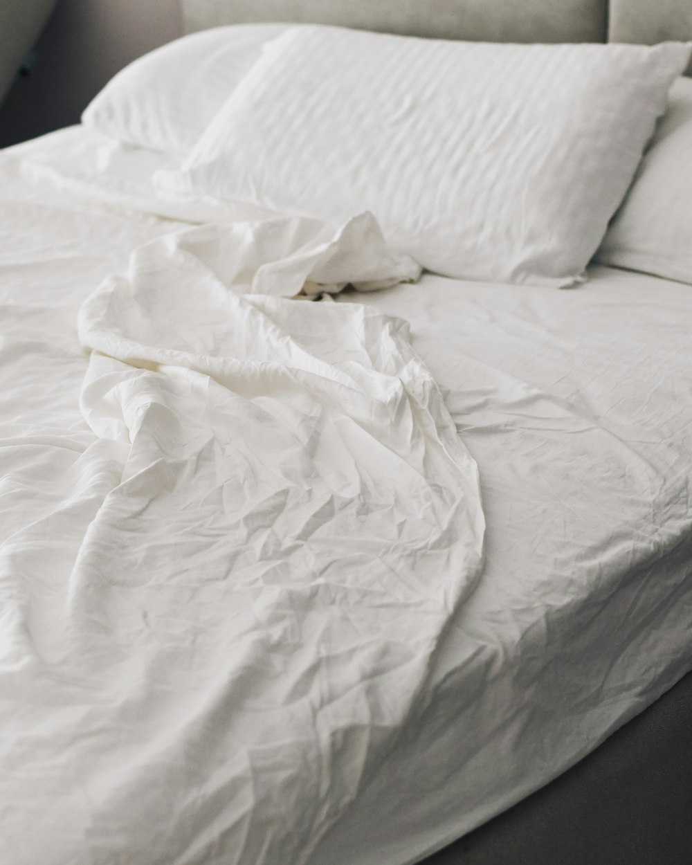 A rumpled white bed and pillows in soft light