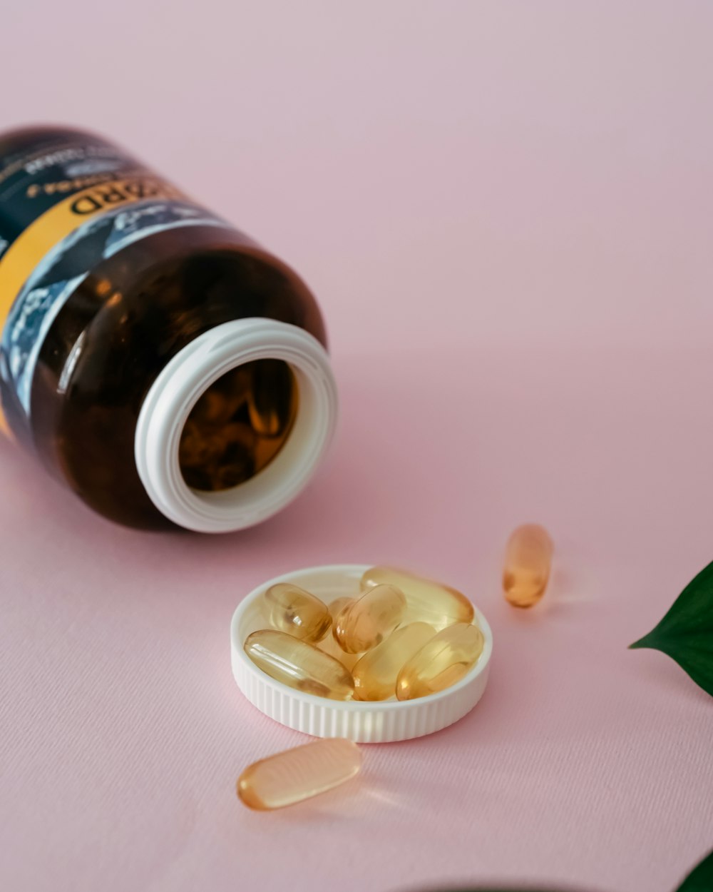 An amber supplement bottle tipped over on a blush background