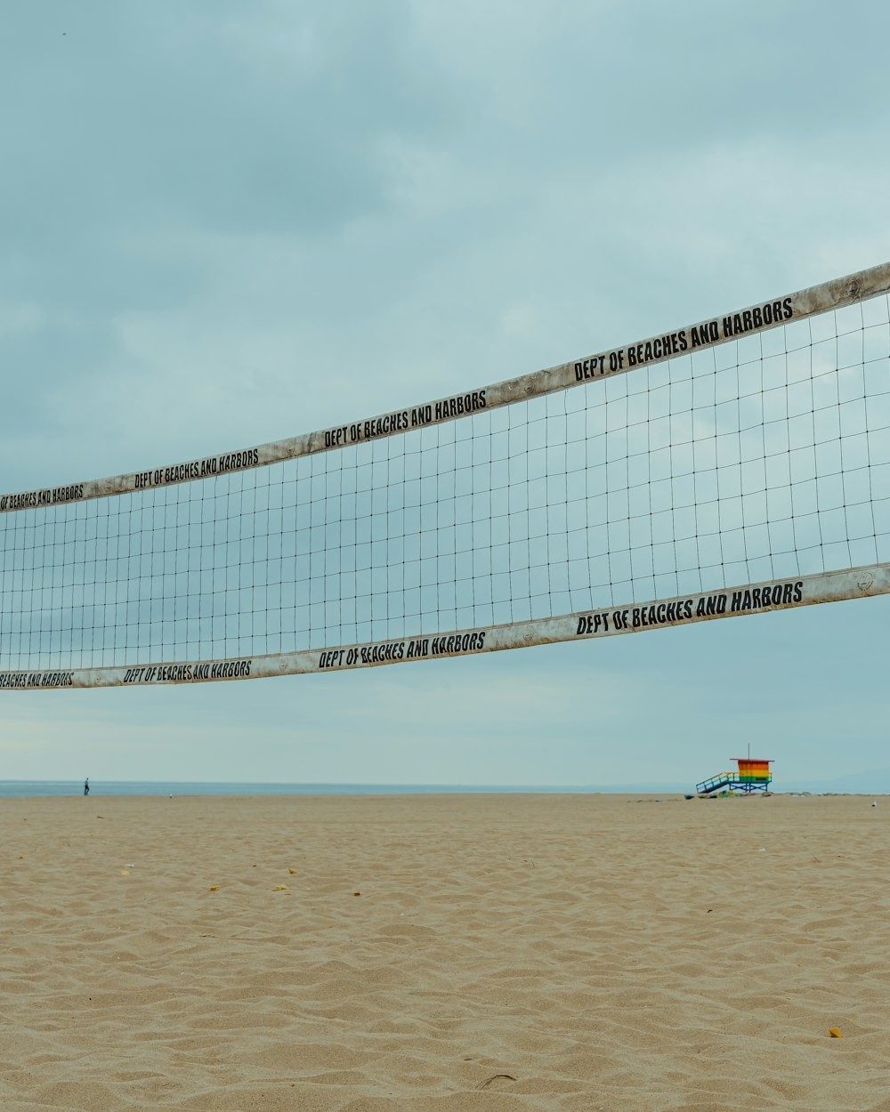 An empty beach volleyball net under an overcast sky
