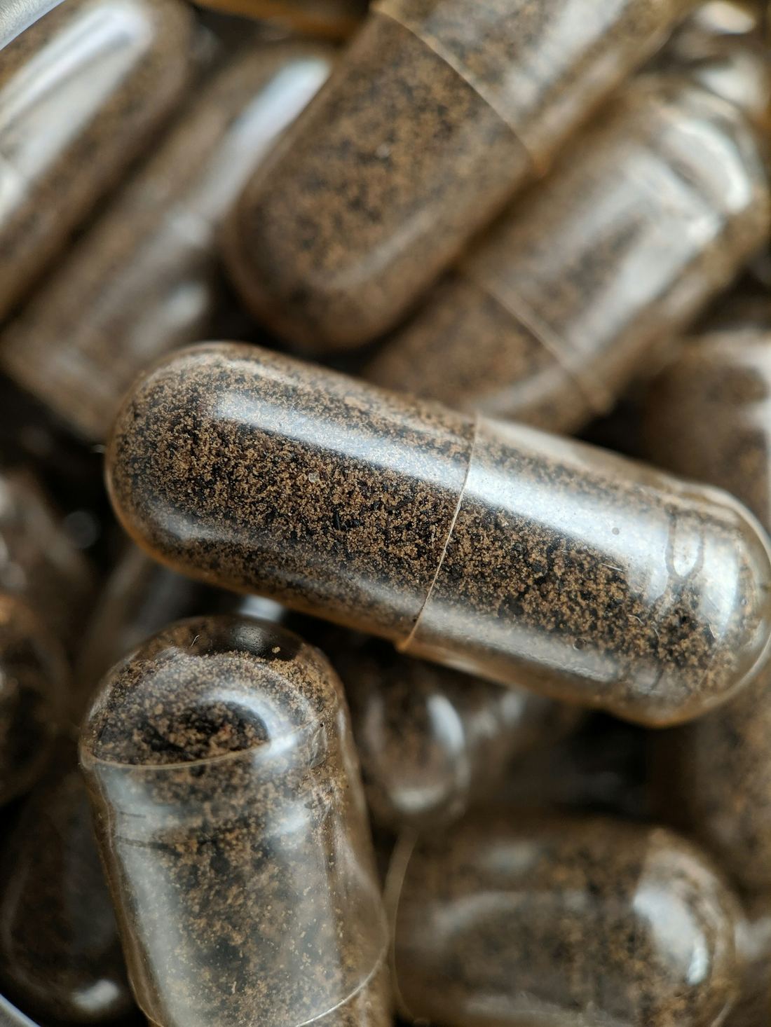 Macro photograph of clear capsules filled with dark ground herbs