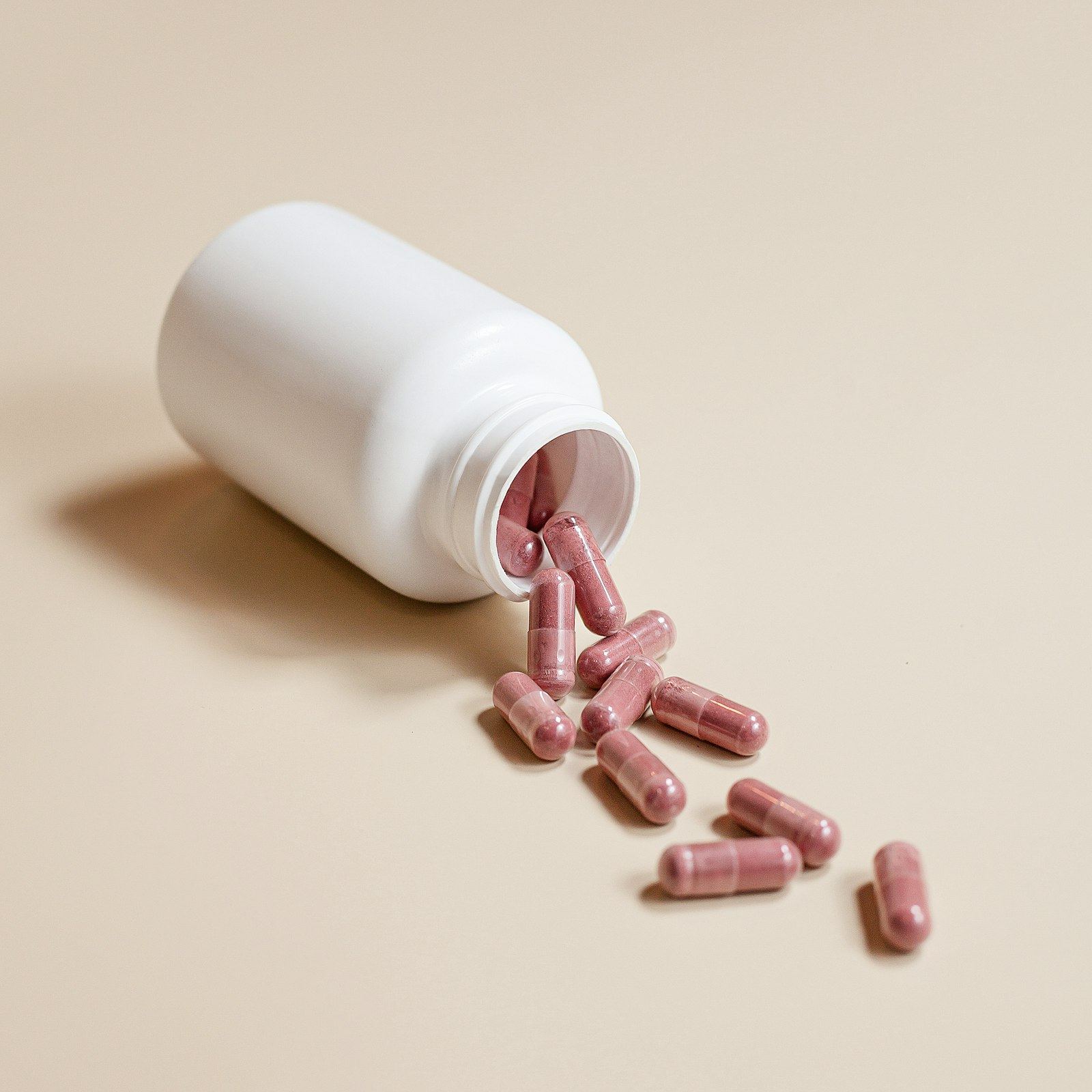 Pink capsules spilling from a white supplement bottle