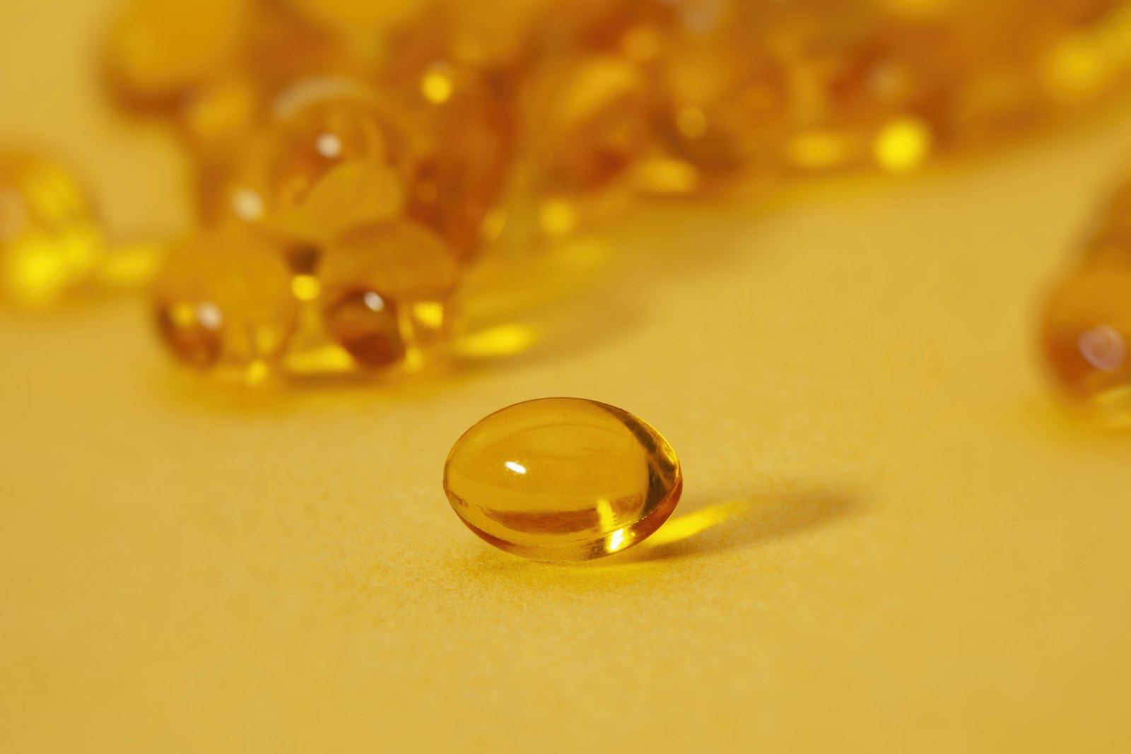 A single amber softgel in front of a pile of others