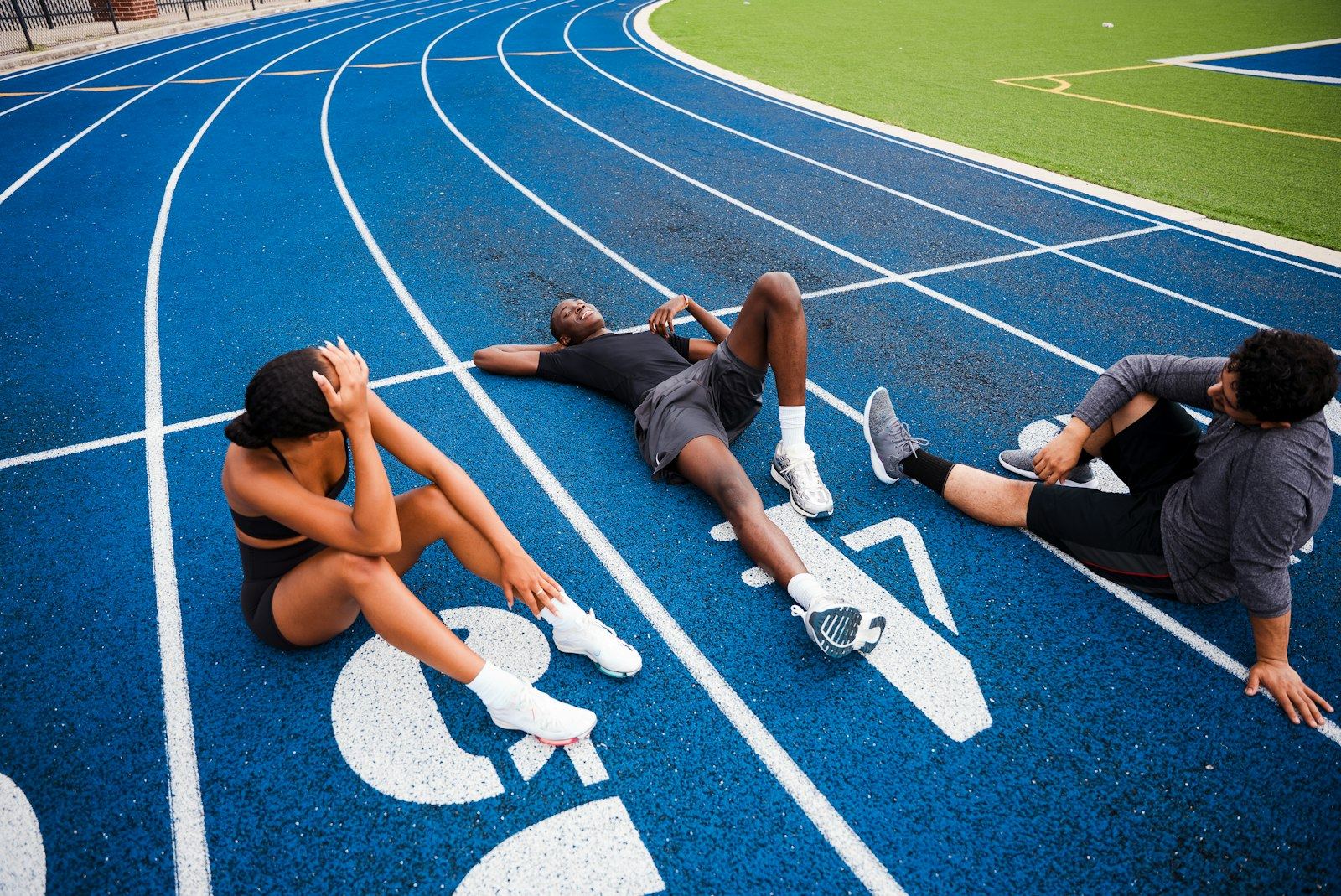 Three runners sitting and lying on a blue track after a hard session