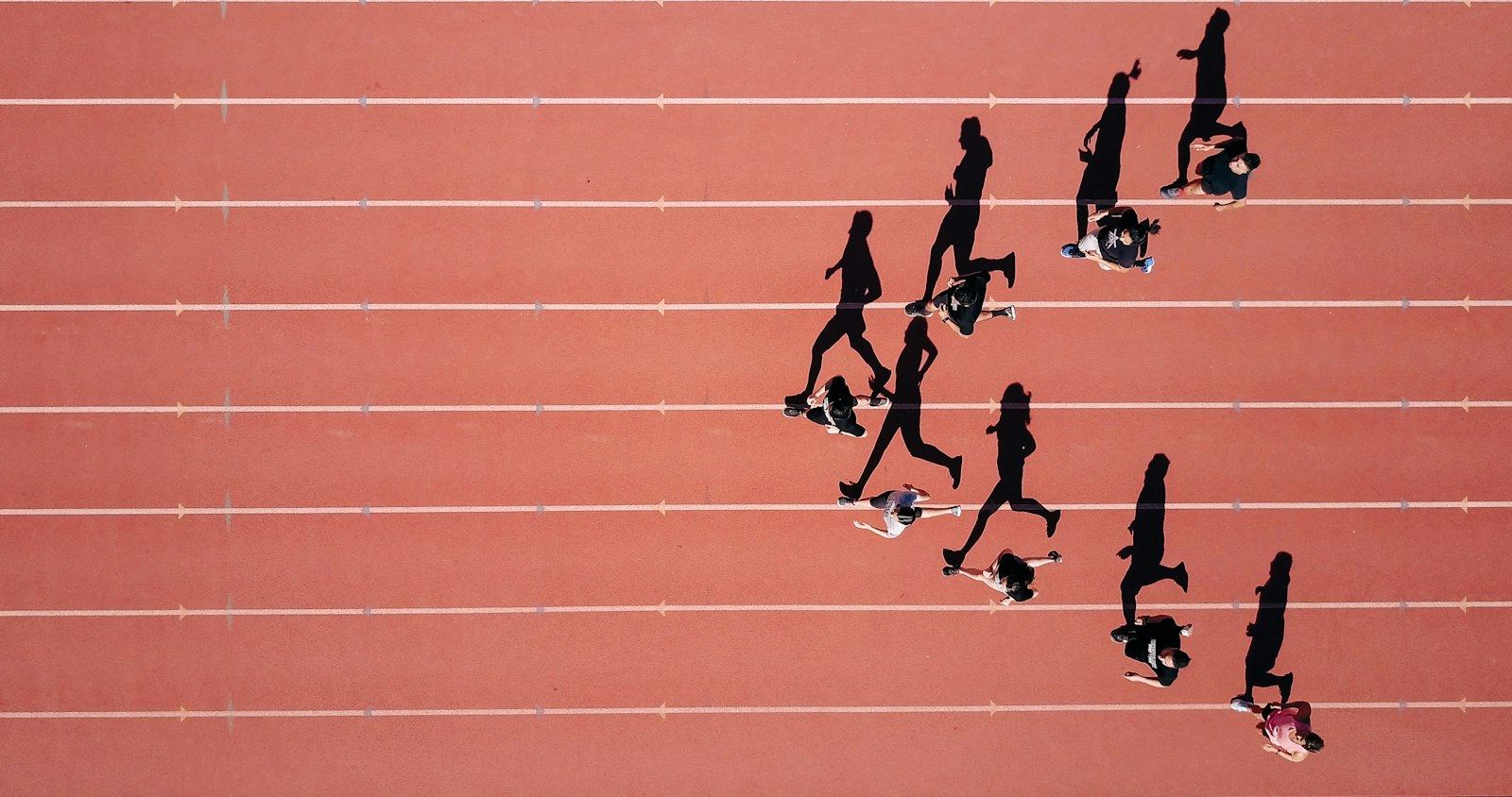 Sprinters seen from directly above, their shadows stretched across a red running track
